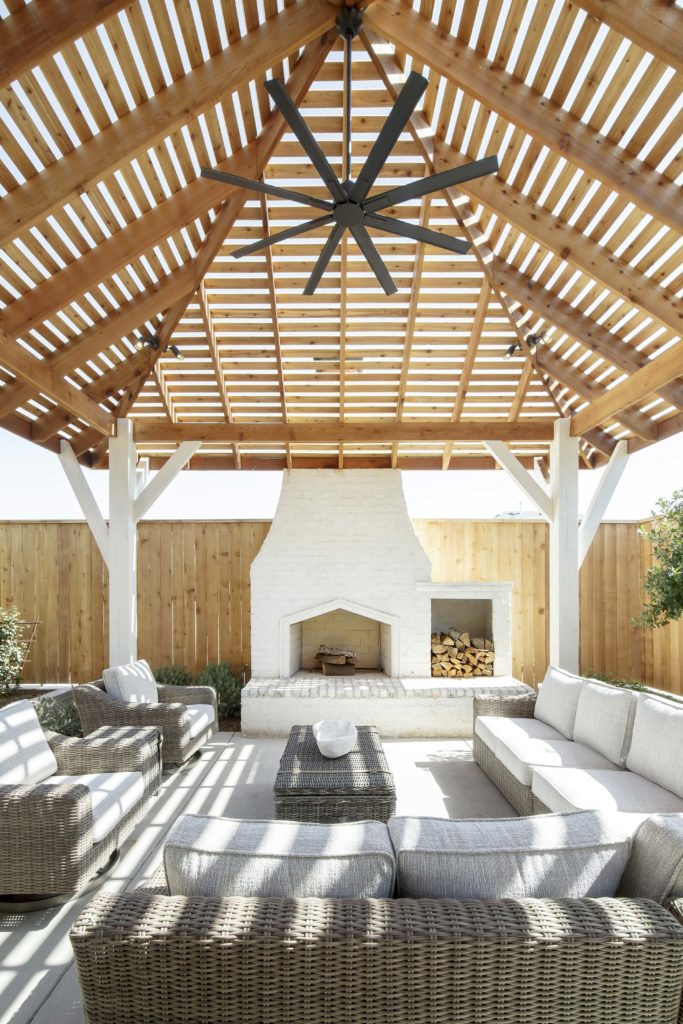 Backyard patio with living area under a pergola with a ceiling fan and fireplace